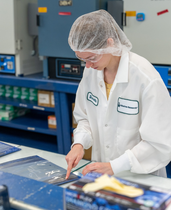 Person in a white lab coat inspecting tapes in the Adhesives Research facility.